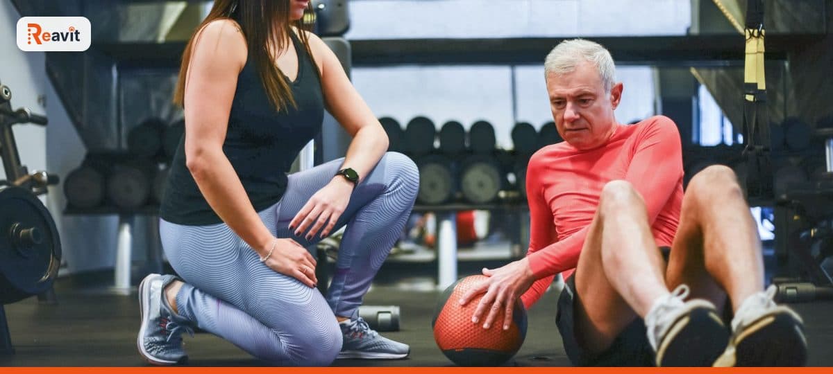 Personal trainer acompanhando aluno sênior durante exercício no solo na academia