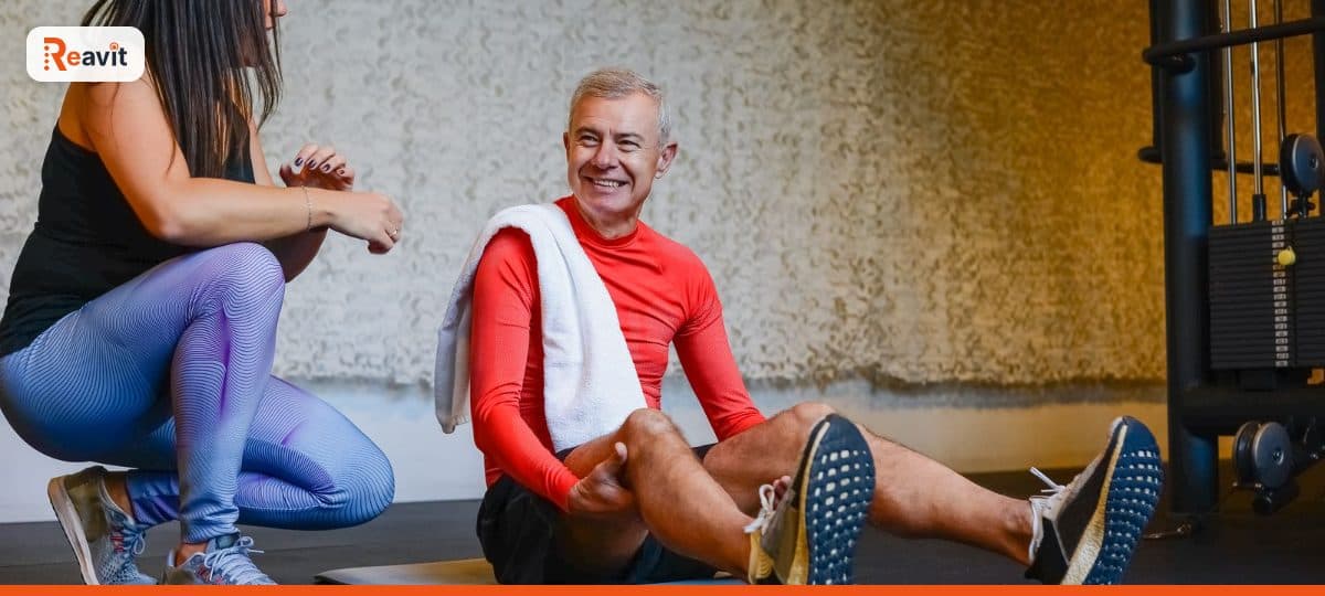Personal trainer conversando com aluno sentado no tapete durante treino na academia